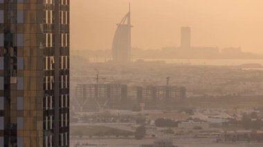 Gün batımında Dubai Su Kanalı 'nın ufuk çizgisindeki inşaat alanı, villalar ve ünlü otel manzarası. Camdan yüzeyi olan gökdelen tarafından çerçevelenmiş