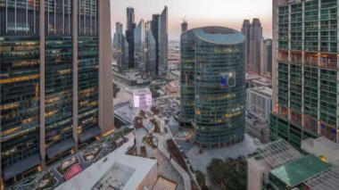 Dubai Uluslararası Finans Merkezi gökdelenleri hava gününden geceye geçiş zamanı. Yukarıdan panoramik manzaralı, aydınlık kuleler ve gezinti güvertesi