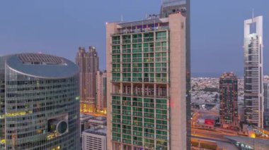 Dubai Uluslararası Finans Merkezi gökdelenleri gece gündüz geçiş zamanları. Aydınlatılmış kuleler güneş doğmadan önce yol trafiğiyle yukarıdan görünürler