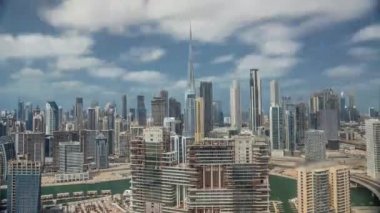 Dubai 'nin panoramik ufuk çizgisi, iş sahası ve şehir merkezi zaman çizelgesi tüm gün boyunca. Bulutlu mavi gökyüzü olan birçok modern gökdelenin havadan görünüşü. Birleşik Arap Emirlikleri.