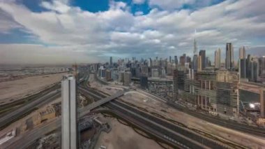 Dubai 'nin panoramik silueti, iş sahasında ve şehir merkezindeki uzun gölgeli zaman çizelgesiyle. Bulutlu mavi gökyüzü olan birçok modern gökdelenin havadan görünüşü. Birleşik Arap Emirlikleri.