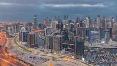 Dubai 'nin modern mimarisine sahip Skyline, gece gündüz geçiş zamanı kulelerini aydınlattı. Güneş doğmadan önce kanal ve şantiyeli havadan panoramik görüntü