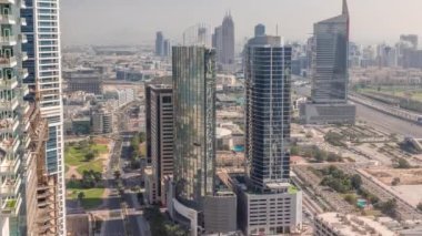 Dubai marinasından tüm gün boyunca medya şehrinin ve Al Barsha Tepeleri 'nin hava görüntüsü. Gölgeli kuleler ve gökdelenler hızla ilerliyor ve yukarıdan bir otoyolda trafik var.