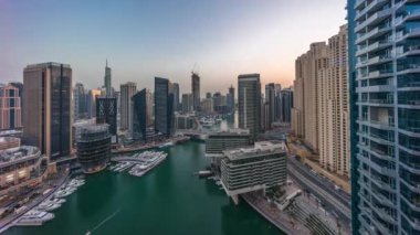Kanal çevresindeki Dubai marina gökdelenlerinin hava panoramik görüntüsü. Günbegün yüzen tekneler ve geçiş zamanı. Günbatımından sonra beyaz tekneler yat kulübüne park edilir.