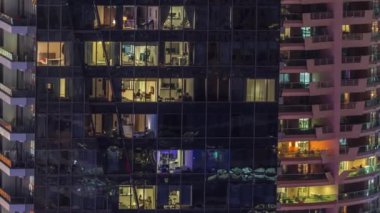 Modern ofisteki pencere ışıkları ve gece vakti balkonlu binalar. İçinde aydınlık odalar olan çok katlı gökdelenler.