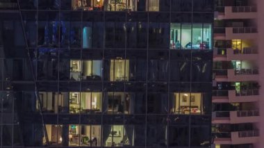 Modern ofisteki pencere ışıkları ve geceleri konut binaları. Çok katlı gökdelenlerin içinde aydınlık odalar ve cam yüzeyden yansımalar var.