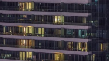 Geceleri modern binalardaki pencere ışıkları zaman ayarlı. İçinde aydınlık odalar olan çok katlı gökdelenler.