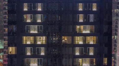 Modern ofisteki pencere ışıkları ve geceleri konut binaları. İçinde aydınlık odalar olan çok katlı gökdelenler. Balkonda birkaç sandalye.