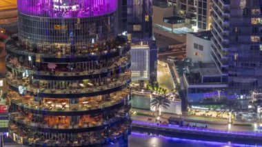 Dubai marinası rıhtımı ve her katta farklı restoranlar bulunan bir bina tüm gece boyunca. Rıhtımı olan yatlar ve ışıkları sönen gökdelenler.