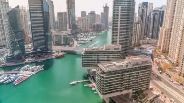 Dubai marinasına ve kanalın etrafındaki JBR gökdelenlerine tüm gün boyunca yüzen tekneler ve uzun gölgeler arasında hızla hareket eden hava manzarası. Yat kulübünde beyaz tekneler var.