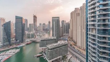 Kanal çevresindeki Dubai marina gökdelenlerinin hava görüntüsü. Günbegün yüzen tekneler ve gece geçiş zamanları. Günbatımından sonra beyaz tekneler yat kulübüne park edilir.