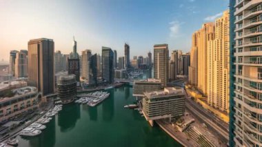 Kanal etrafındaki Dubai marina gökdelenlerinin hava panoramik görüntüsü gün doğumunda yüzen teknelerle birlikte. Yat kulübünde beyaz tekneler var.