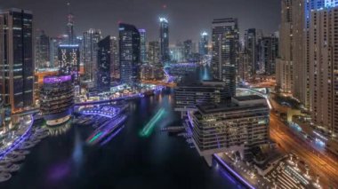 Dubai marinasının hava panoramik görüntüsü kanalın etrafındaki gökdelenleri aydınlatıyor ve yüzen yatlar tüm gece boyunca zaman ayarlı ve ışıklar kapanıyor. Yat kulübünde beyaz tekneler var.
