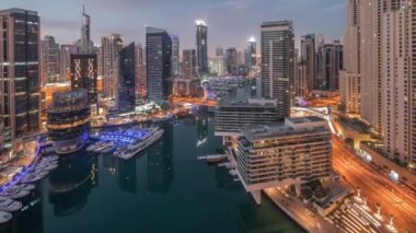 Dubai marinasına ve kanalın etrafındaki gökdelenleri gece gündüz yüzen yatlarla aydınlatan hava manzarası. Güneş doğmadan önce beyaz tekneler yat kulübüne park edilir.