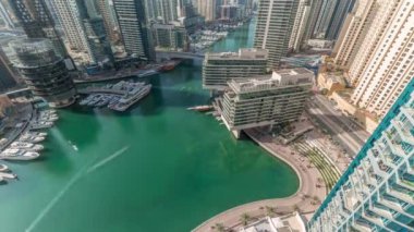 Kanal etrafındaki Dubai marina gökdelenlerine havadan bakıldığında gölgeler hızla ilerlerken yüzen teknelerin zamanlaması görülüyor. Beyaz tekneler yat kulübüne ve alışveriş merkezinin yakınına park edilmiş.