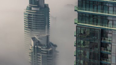 Dubai Marina ufuk çizgisi üzerinde nadir bulunan kış sisi ve hava saatleri üzerinde cam gökdelenlerle kaplı kuleler. Üst görünüm bulutların üstünde. Dubai, BAE