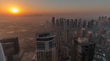 Dubai Marina Panoraması 'nda güneş doğarken JLT gökdelenleri ve golf sahası, Dubai, Birleşik Arap Emirlikleri. Yukarıdan hava manzarası sisli bir sabah. Turuncu gökyüzü ile şehir silueti