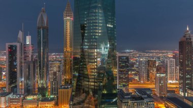 Dubai 'nin finans merkezi, gece gündüz aydınlık lüks gökdelenler geçiş zamanı, Dubai, Birleşik Arap Emirlikleri. Pencerelerde ve ofis kulelerinde ışık olan hava manzarası