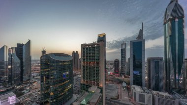 Dubai Uluslararası Finans Merkezi gökdelenleri hava gününden geceye geçiş zamanı. Aydınlatılmış kule manzaralı bir otoyol trafiği