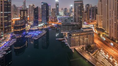 Dubai marinasına ve kanalın etrafındaki gökdelenleri gece gündüz yüzen yatlarla aydınlatan hava manzarası. Güneş doğmadan önce beyaz tekneler yat kulübüne park edilir.