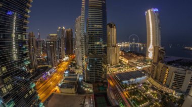 Dubai Marina ve JBR bölgesinin panoraması ve ünlü Ferris Wheel gece gündüz geçiş zamanı. Gün doğumunda uzun gölgelerle aydınlatılmış gökdelenler