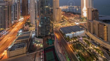 Dubai Marina ve JBR bölgesinin panoramik görüntüsü ve ünlü dönme dolabın gece gündüz geçiş zamanı. Gün doğumunda uzun gölgelerle aydınlatılmış gökdelenler