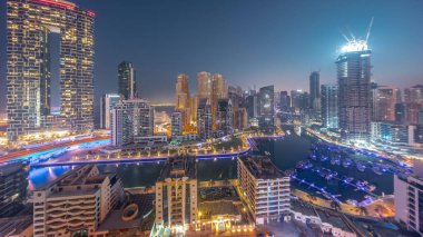 Dubai Marina Panoraması 'nda limana parkedilmiş tekne ve yatlar ve gün doğumundan önce gece gündüz kanal havası etrafında aydınlık gökdelenler var. Arka planda JBR bölgesi kuleleri