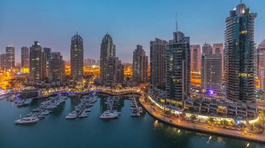 Gündoğumundan önce Dubai marinasında gece gündüz lüks yat hangarında geçiş zamanı. Rıhtım boyunca modern gökdelenler ve limanda yüzen tekneler.