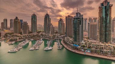 Dubai Marina turizm bölgesi üzerinde gündoğumu. Gökdelenler ve kanalın çevresindeki panoramik zaman çizelgeleri. Residential binalar ve caddelerdeki trafik
