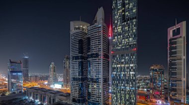 Panorama, Dubai Uluslararası Finans Bölgesi 'nin gökdelenler tarafından aydınlatılmış gece zaman çizelgesini gösteriyor. Çok katlı otoparkların yakınındaki bir yolda trafik vardı. Dubai, BAE.