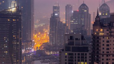 Dubai Marina ve Media City semtleri modern gökdelenler ve ofis binaları gece gündüz geçiş zamanları. Limandaki yatların yakınındaki üst geçitte trafik ve kavşak.
