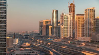 Dubai Marina 'da gökdelenler üzerinde uzun gölgeler ve gün doğumunda metro raylı Şeyh Zayed yolu. Modern kulelerin yakınındaki bir otoyolda trafik var, Birleşik Arap Emirlikleri