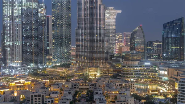 Dubai Downtown night to day transition timelapse with tallest skyscraper and other illuminated towers view from the top before sunrise, United Arab Emirates. Traditional houses of old town and shopping mall