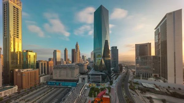 Dubai International Financial district after sunrise aerial timelapse. Panoramic view of business and financial office towers with long shadows. Skyscrapers with parking lot and shopping mall near downtown