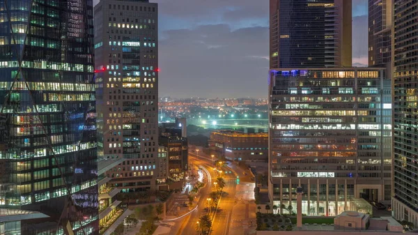 Dubai International Financial district night to day transition timelapse. Aerial view of business office towers before sunrise. Illuminated skyscrapers with road traffic and Deira district on a background