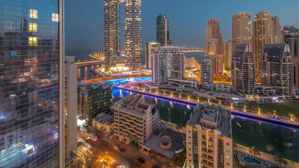 Dubai Marina skyscrapers and JBR district before sunrise with illuminated luxury buildings and resorts aerial night to day transition timelapse. Waterfront with palms and boats floating in canal