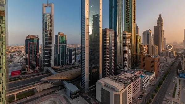 Aerial view of Dubai International Financial District with sun reflected from skyscrapers during sunrise timelapse. Traffic on a road near multi storey parking with rooftop swimming pool. Dubai, UAE.