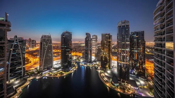 Tall residential buildings panorama at JLT district aerial night to day transition timelapse, part of the Dubai multi commodities centre mixed-use district. Illuminated towers and skyscrapers