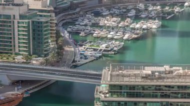 Kanal çevresindeki Dubai marina gökdelenlerine doğru yüzen botların zaman ayarlı görüntüsü. Beyaz tekneler yat kulübüne park edilmiş. Sabah hareket eden gölgelerle dolu bir köprüde trafik vardı.