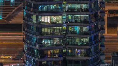 Gece vakitlerinde apartmanların pencereleri, evlerin pencerelerinden gelen ışık. Parlak odalı şehrin akşam manzarası. Gökdelenin arkasındaki trafik