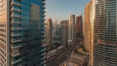 Dubai Marina ve JBR bölgesi ve caddelerdeki trafik sabah saatleri ve güneş gün doğumunda sisli gökdelenlerden yansıyor.