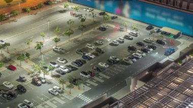 Top view otoparkı, gece vakti bir sürü araba gelip gidiyor. Yukarıdan hava manzaralı, alışveriş merkezinin yakınında bir taksi var.