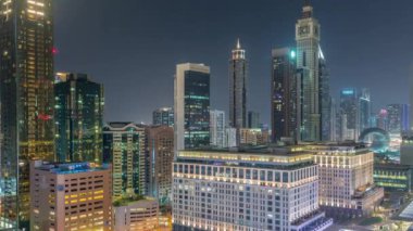 Tüm gece boyunca Dubai Uluslararası Finans Bölgesi. İş yeri kulelerinin havadan görüntüsü. Işıklar sönerken aydınlatılmış gökdelenler