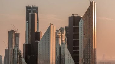 Dubai 'nin finans bölgesindeki ofis kulelerinin cam yüzeyinden yansıyan güneş. Güneş batarken arkasında inşaat alanı olan turuncu ışıkla hava manzarası
