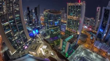 Dubai Uluslararası Finans Merkezi gökdelenlerinin panoraması tüm gece boyunca geçit caddesi gezinti alanı ve camii ile havadan zamanlaması. Yukarıdan aydınlatma kuleleri görünümü