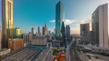 Güneş doğduktan sonra Dubai Uluslararası Finans Bölgesi. İş dünyasının panoramik manzarası ve uzun gölgeli finans kuleleri. Otoparkı ve alışveriş merkezi olan gökdelenler