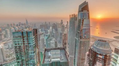 Dubai Marina 'nın gün batımı manzarası kıyı şeridi boyunca gökdelenlerle çevrili yapay bir kanal gösteriyor. Modern kulelerin üzerinde turuncu gökyüzü. Dubai, BAE