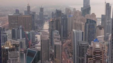 Dubai Marina 'nın gökdelenlerle çevrili bir kanalı gösteren Skyline manzarası. Sahil şeridi boyunca, hava gününden gece geçiş zamanına kadar. Gün batımından sonra yüzen yatlar ve tekneler. Dubai, BAE