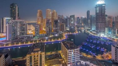 Limanda park etmiş tekne ve yatları olan Dubai Marina ve gün doğumundan önce gece gündüz kanal havası etrafında gökdelenler aydınlatılıyor. Arka planda JBR bölgesi kuleleri