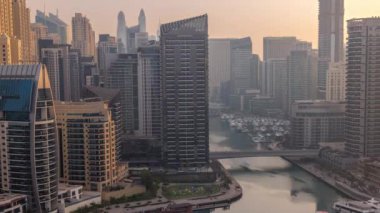Dubai Marina 'da limanda tekneleri ve yatları var. Gün doğumunda kanalın etrafında gökdelenler var. Ilık ışıklarla dolu kuleler.